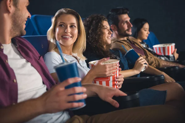 Cheerful multiethnic friends with popcorn watching film together in movie theater — Stock Photo