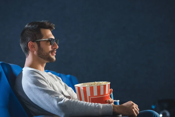 Vue latérale du jeune homme en 3d lunettes avec pop-corn regarder le film au cinéma — Photo de stock