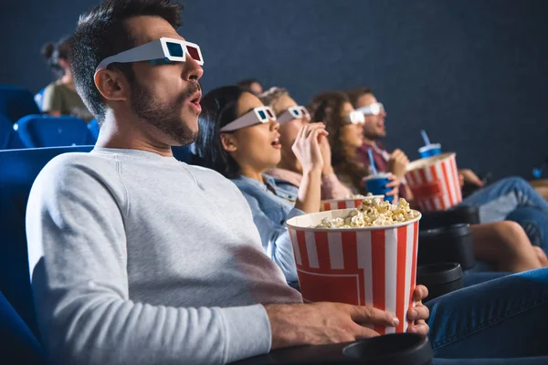 Shocked multiethnic friends in 3d glasses with popcorn watching film together in movie theater — Stock Photo