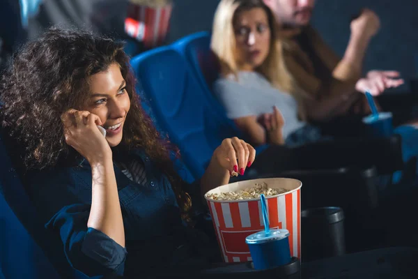Mujer con palomitas de maíz hablando en el teléfono inteligente mientras ve películas en el cine - foto de stock