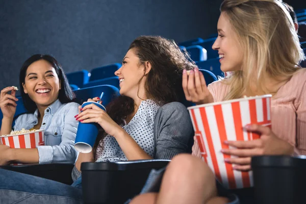 Heureuses femmes multiraciales avec du pop-corn regardant un film ensemble au cinéma — Photo de stock