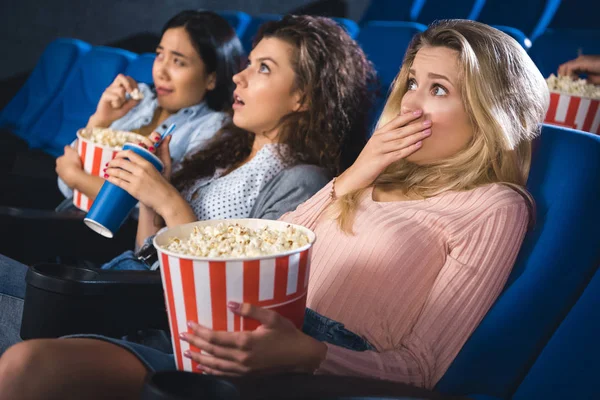 Spaventate donne multirazziali con popcorn che guardano film insieme nel cinema — Foto stock