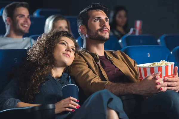 Young couple with popcorn holding hands while watching movie together in cinema — Stock Photo