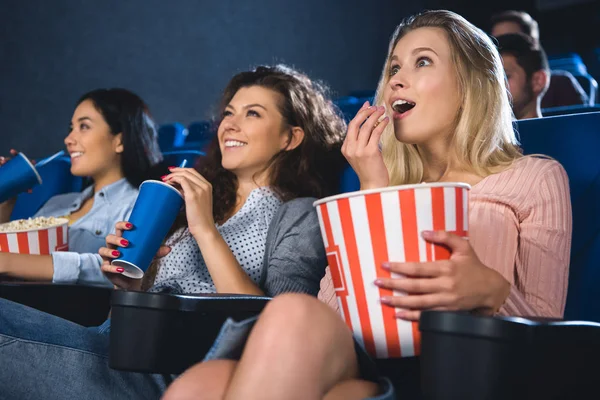 Mujeres multirraciales emocionales con palomitas de maíz viendo películas juntas en el cine - foto de stock