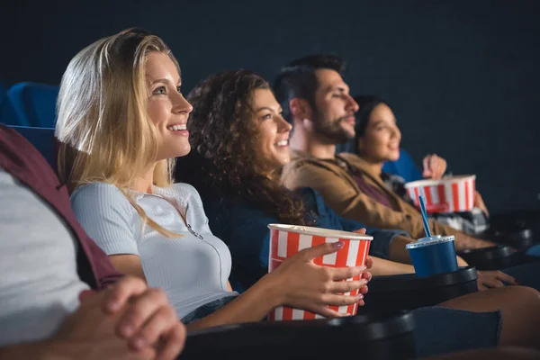 Sonrientes amigos multiétnicos con palomitas de maíz viendo películas juntos en el cine - foto de stock