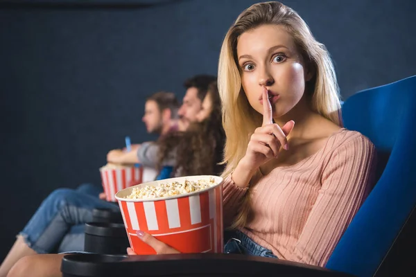 Selective focus of woman with popcorn showing silence sign in cinema — Stock Photo
