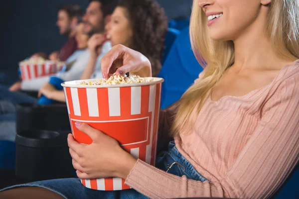 Partial view of multiethnic friends with popcorn watching film together in movie theater — Stock Photo