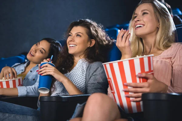 Alegres mujeres multirraciales con palomitas de maíz viendo películas juntas en el cine - foto de stock