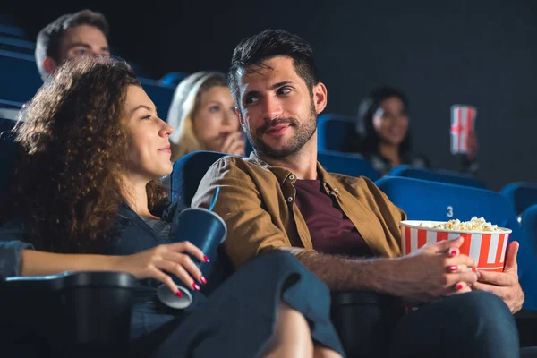 Couple with popcorn holdnig hands while watching movie together in cinema — Stock Photo