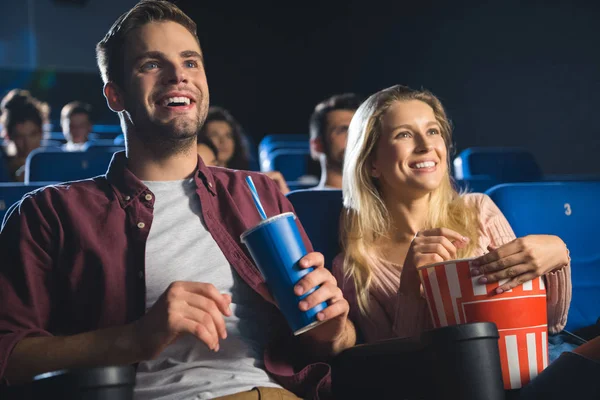 Cheerful couple with popcorn and soda drink watching film together in cinema — Stock Photo