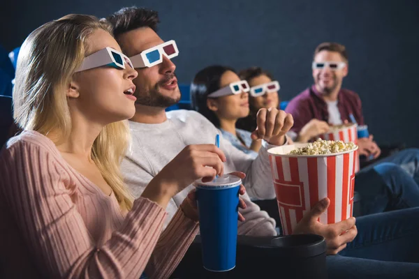 Amigos multiétnicos en gafas 3D con palomitas de maíz viendo películas juntos en el cine - foto de stock