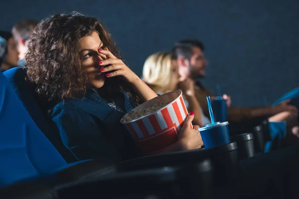 Испуганная женщина с попкорном закрывая глаза во время просмотра фильма в кино — стоковое фото