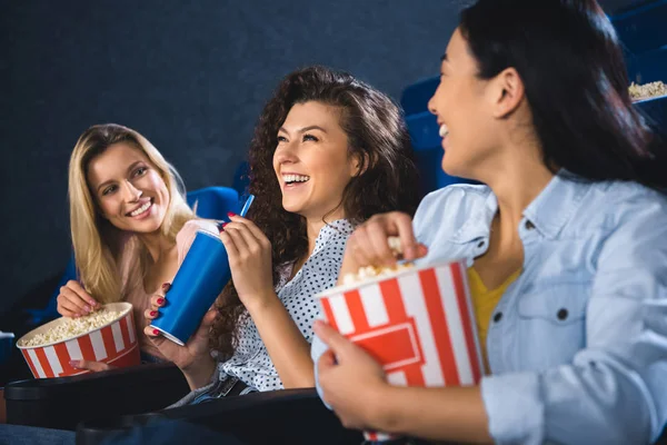 Веселі багаторасові жінки з попкорном дивитися фільм разом у кінотеатрі — стокове фото