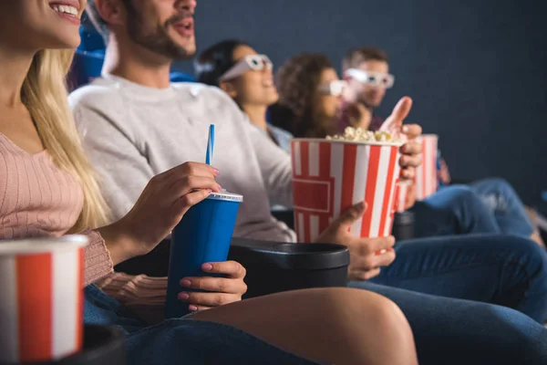 Vue partielle d'amis émotionnels multiethniques avec du pop-corn regardant un film ensemble dans un cinéma — Photo de stock