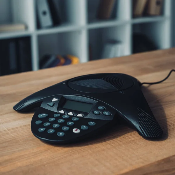 Speakerphone on wooden table at office with blurred bookshelves on background — Stock Photo
