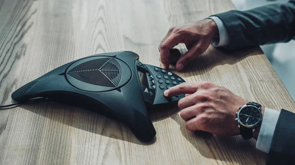 Cropped shot of businessman pushing button of conference phone on table — Stock Photo