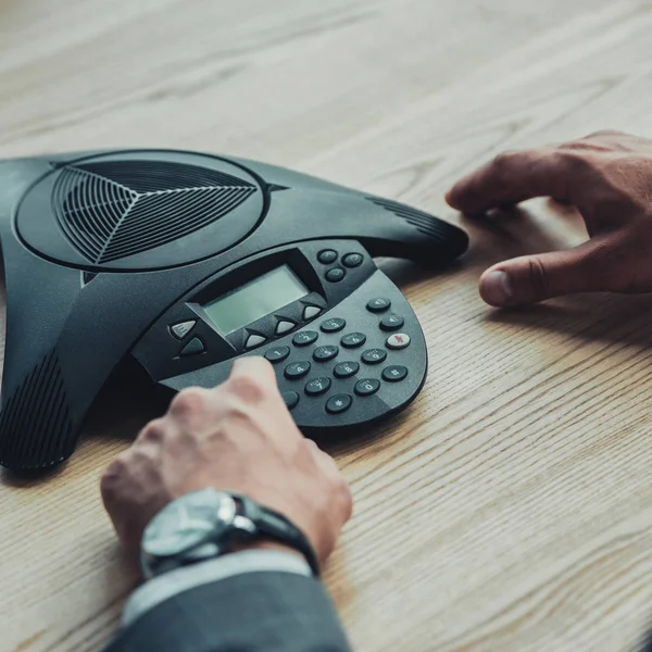 Cropped shot of businessman pushing button of conference phone at workplace in office — Stock Photo