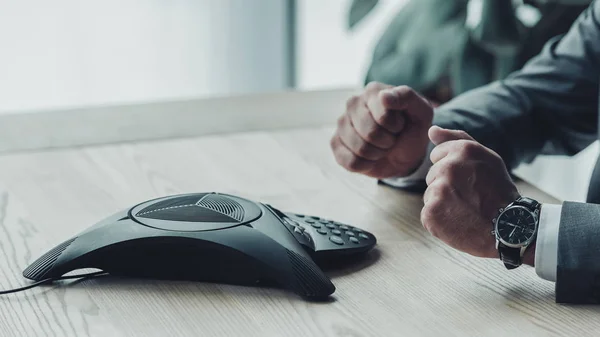 Cropped shot of businessman sitting in front of conference phone and making fists at office — Stock Photo