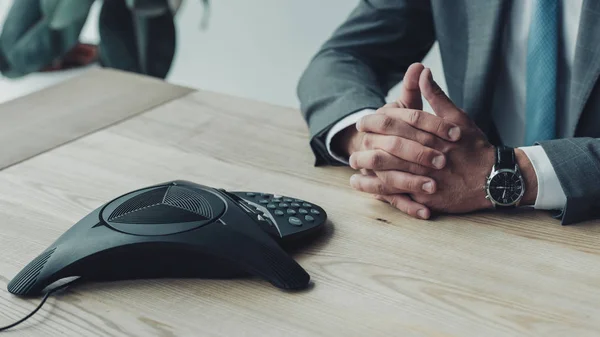 Cropped shot of businessman sitting at workplace with conference phone — Stock Photo