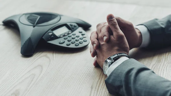 Cropped shot of businessman in suit sitting in front of conference phone on table at office — Stock Photo