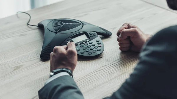 Cropped shot of angry businessman sitting in front of conference phone and making fists at office — Stock Photo