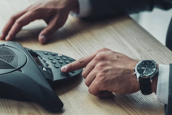 Cropped shot of businessman in suit pushing button of conference phone on table at office — Stock Photo