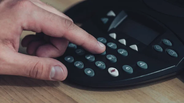 Cropped shot of man pushing button of conference phone on wooden table — Stock Photo