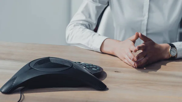 Cropped shot of businesswoman in white shirt sitting in front of conference phone and waiting for call — Stock Photo