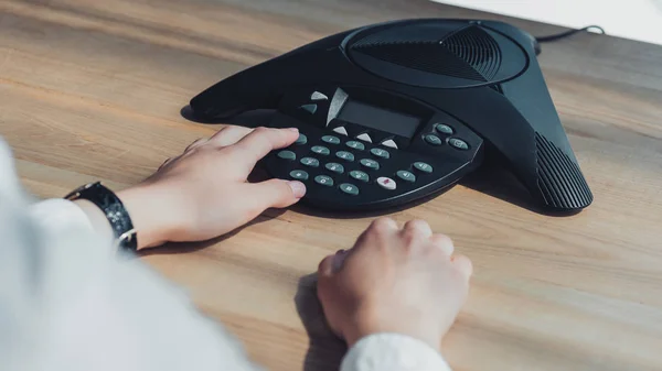 Cropped shot of businesswoman pushing button of conference phone on table at office — Stock Photo