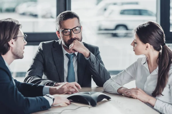 Thoughtful serious business people using conference phone at modern office — Stock Photo