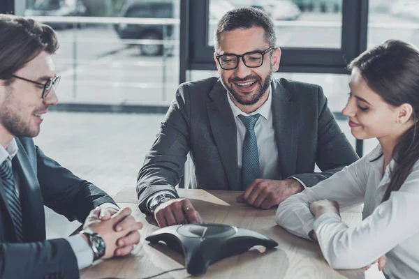 Zufriedene Geschäftsleute mit Konferenztelefon im modernen Büro — Stockfoto