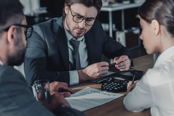 Serious business people sitting around conference phone at modern office — Stock Photo