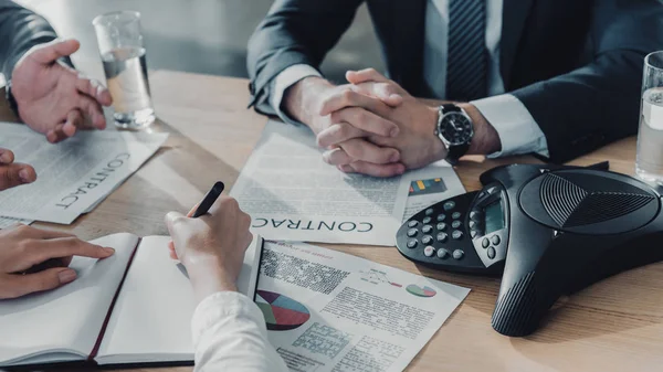 Cropped shot of business people having conversation with documents and speakerphone on table at modern office — Stock Photo