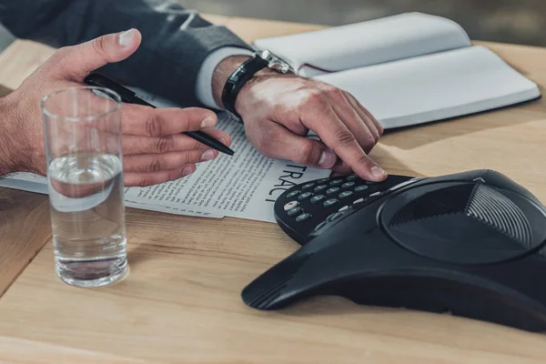 Colpo ritagliato di uomo d'affari utilizzando il telefono conferenza sul tavolo in ufficio — Foto stock