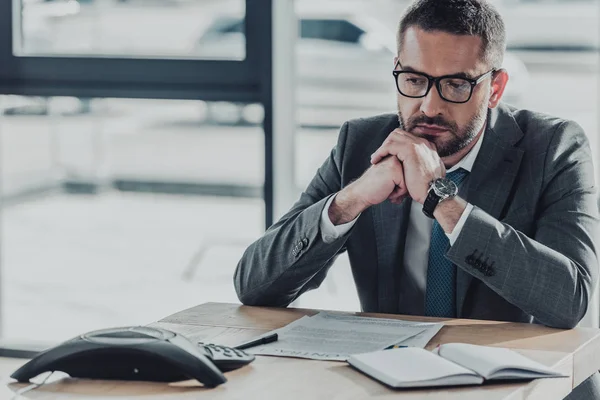 Selbstbewusster Geschäftsmann, der am Arbeitsplatz sitzt und im Büro auf das Konferenztelefon auf dem Tisch schaut — Stockfoto