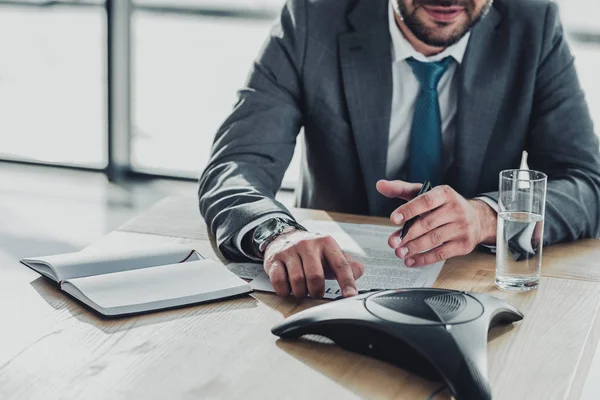 Schnappschuss eines lächelnden Geschäftsmannes mit Konferenztelefon auf dem Tisch im Büro — Stockfoto