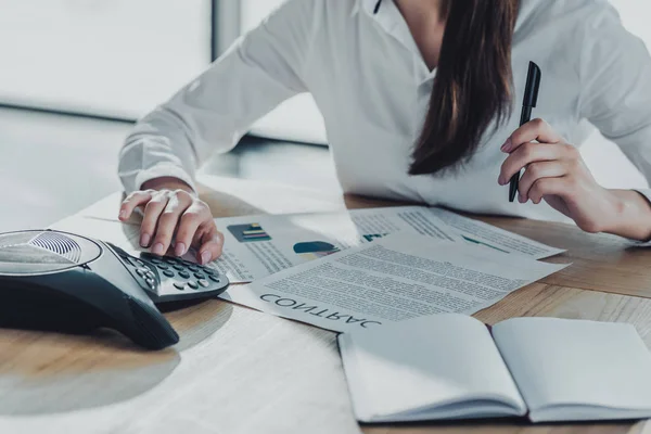 Cropped shot of businesswoman with paperwork using conference phone at office — Stock Photo