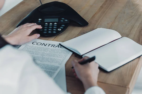 Cropped shot of businesswoman with contract pushing button of conference phone on table at office — Stock Photo