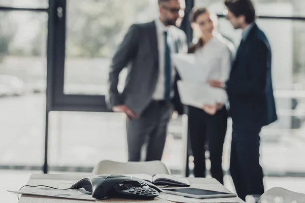 Close-up shot of conference phone with blurred business people on background at office — Stock Photo