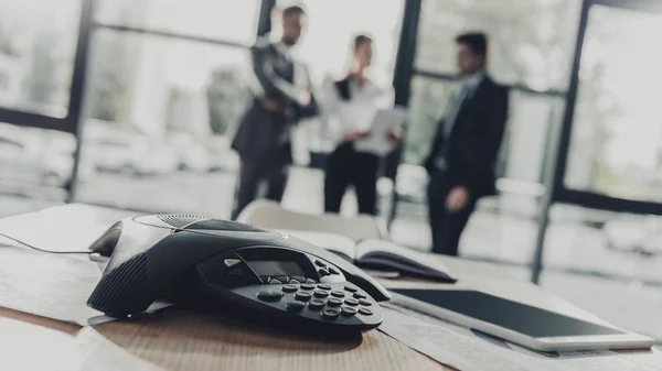 Nahaufnahme eines Konferenztelefons mit verschwommenen Geschäftsleuten im Hintergrund im modernen Büro — Stockfoto