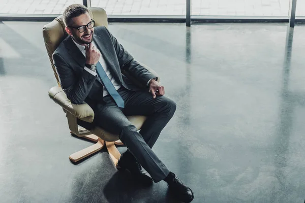 Blick aus der Vogelperspektive auf einen gutaussehenden, glücklichen Geschäftsmann, der im modernen Büro auf einem Luxussessel sitzt — Stockfoto