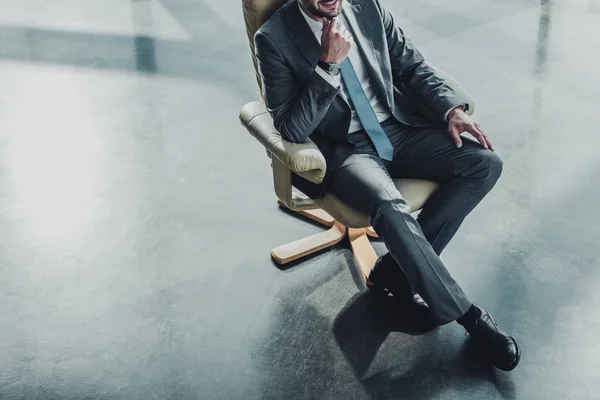 Tiro recortado de hombre de negocios guapo sentado en un sillón de lujo en la oficina moderna - foto de stock