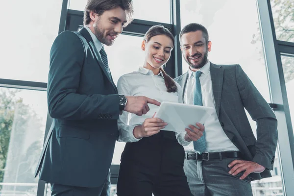 Vista inferior de la gente de negocios feliz utilizando tableta juntos en la oficina moderna - foto de stock