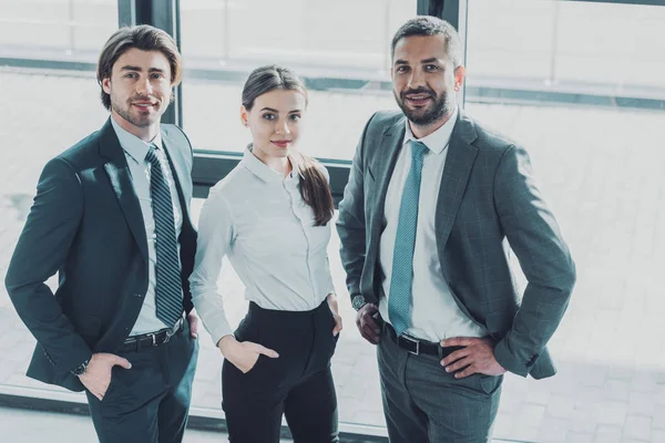 Group of smiling young business people standing at modern office and looking at camera — Stock Photo