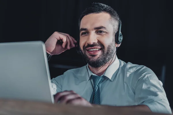 Sonriente trabajador de línea directa de apoyo con portátil y micrófono en el trabajo - foto de stock