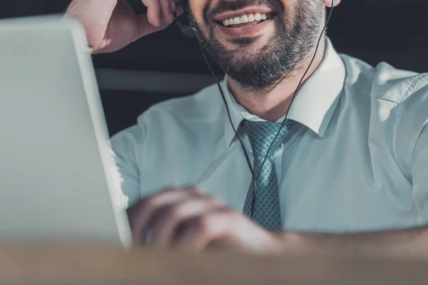 Cropped shot of smiling support hotline worker with laptop and microphone at work — Stock Photo