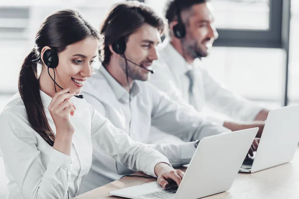 Lächelnde Callcenter-Manager in weißen Hemden arbeiten zusammen, während sie im modernen Büro in der Reihe sitzen — Stockfoto