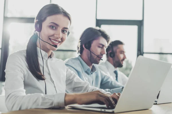 Happy call center managers working with laptops and microphones at modern office — Stock Photo