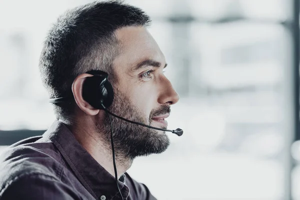 Vista lateral del trabajador guapo del centro de llamadas en auriculares con micrófono - foto de stock