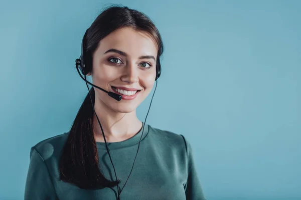 Attraktive lächelnde Callcenter-Mitarbeiterin blickt vereinzelt in die Kamera auf blauem Grund — Stockfoto